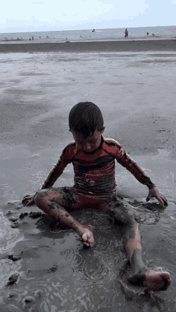 a young boy is playing in the mud on a beach