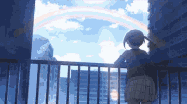 a girl is standing on a balcony looking at a rainbow in the sky .