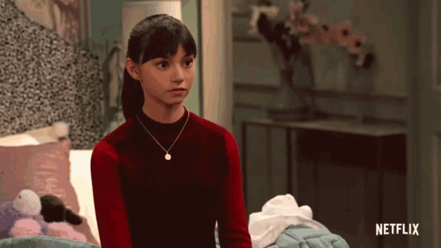 a girl in a red sweater is sitting on a bed with a netflix logo in the corner