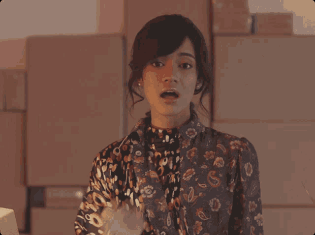 a woman in a floral shirt is standing in front of a stack of cardboard boxes