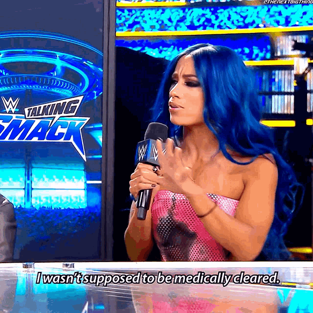 a woman with blue hair is holding a microphone in front of a sign that says talking smack