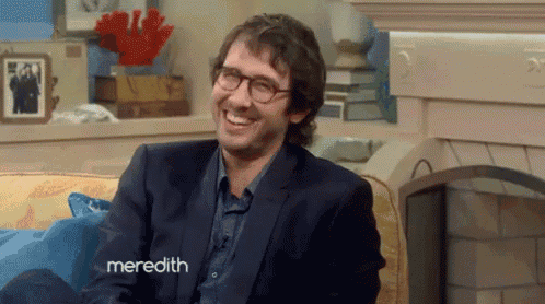 a man in a suit and glasses is sitting on a couch with meredith written on the bottom right