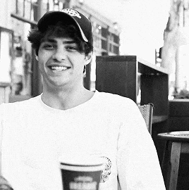 a man wearing a hat and a white shirt is holding a cup of coffee
