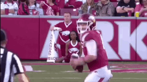 a football player is kneeling down on the field with a cheerleader behind him .