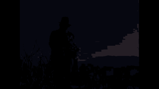 a man in a suit and hat is holding a gun in a field
