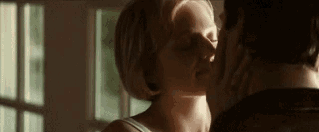 a man and a woman are kissing in front of a window in a room .