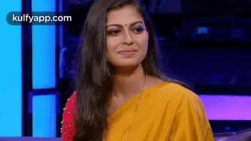 a woman in a yellow and red saree is sitting on a couch .
