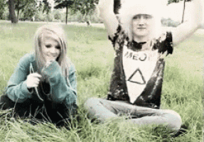 a man and a woman are sitting in the grass with their arms in the air
