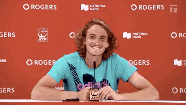 a man sitting at a table with rogers and national bank logos on the wall behind him
