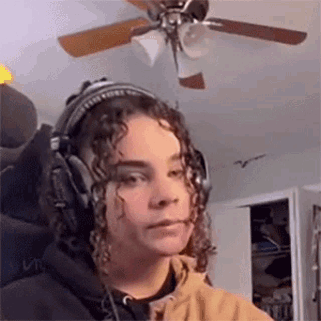 a woman wearing headphones is standing in a room with a ceiling fan in the background .