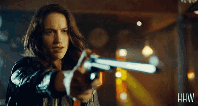 a woman is pointing a gun with the letters hw on the bottom right