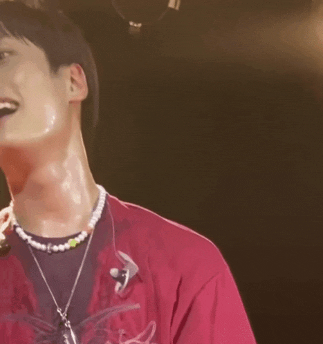 a man wearing a pink shirt and a pearl necklace is smiling
