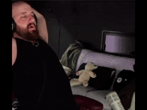 a man with a beard wearing headphones is sitting on a couch with a stuffed animal .