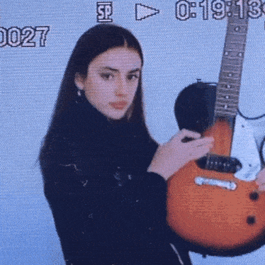 a young woman is holding a guitar in front of a screen that says 0 : 19 : 13
