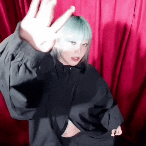 a woman with blue hair and a black jacket is making a peace sign