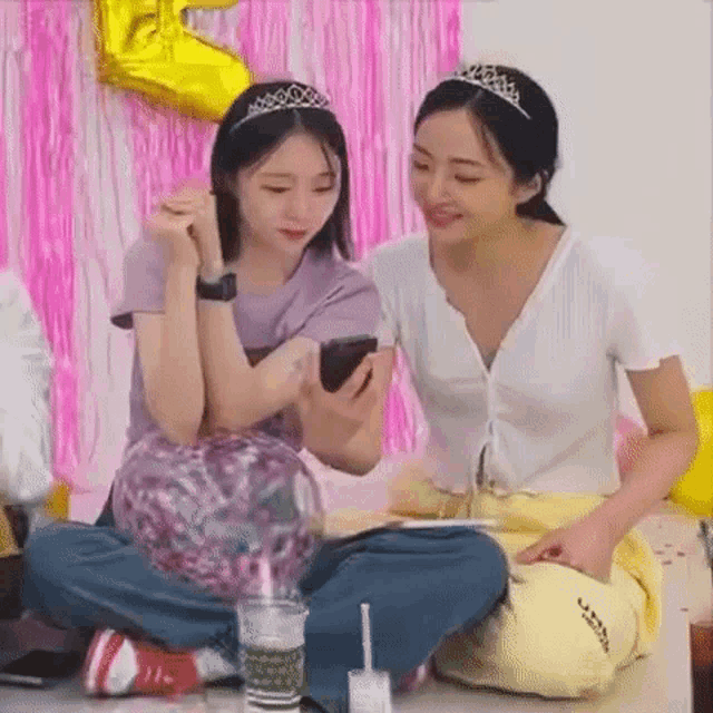 a couple of girls are sitting on the floor looking at a cell phone .