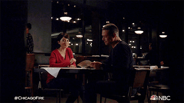 a man and a woman are sitting at a table with #chicagofire written on the bottom of the screen