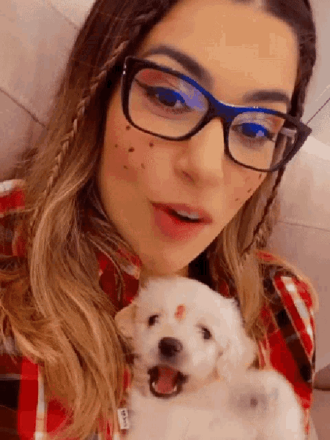 a woman wearing glasses holds a small white puppy