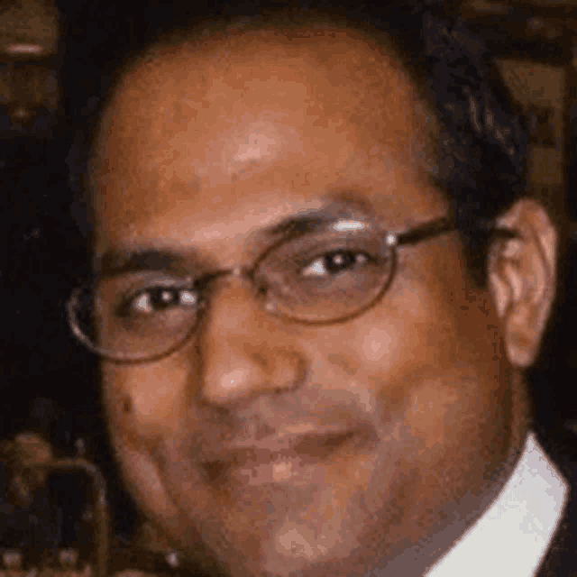 a close up of a man wearing glasses and a suit and tie .
