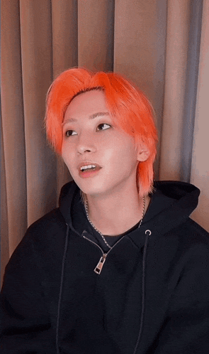 a man with bright orange hair wearing a black hoodie