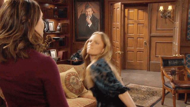 two women are standing in a living room with a picture of a man on the wall behind them