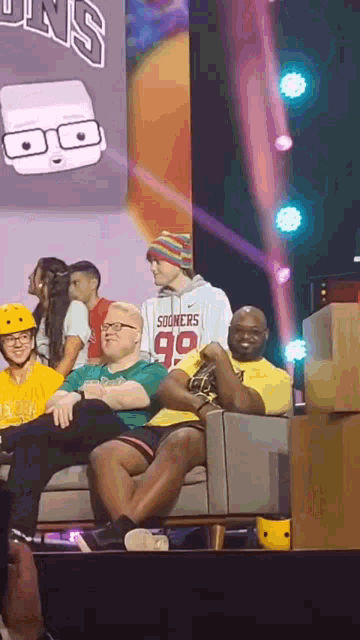 a group of people are sitting on a couch in front of a sign that says sooners