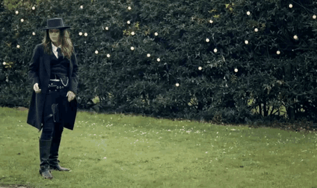 a man in a black coat and hat is standing in a grassy field