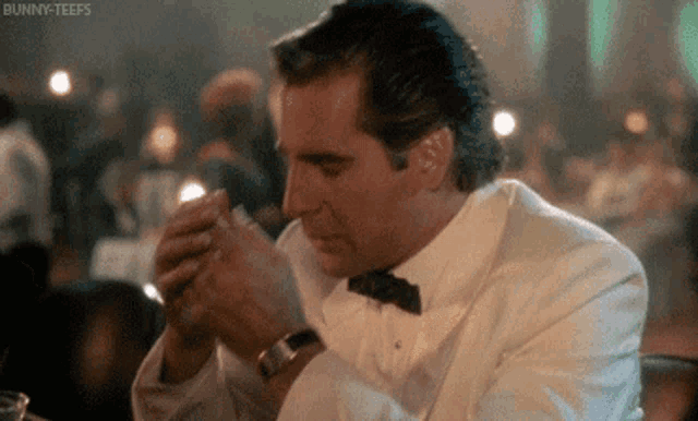 a man in a tuxedo and bow tie is sitting at a table eating a sandwich .