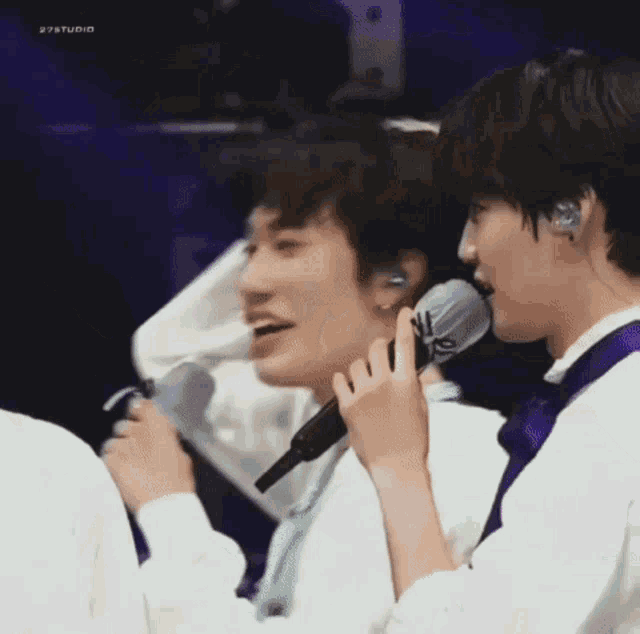 a group of young men are singing into microphones while sitting next to each other .