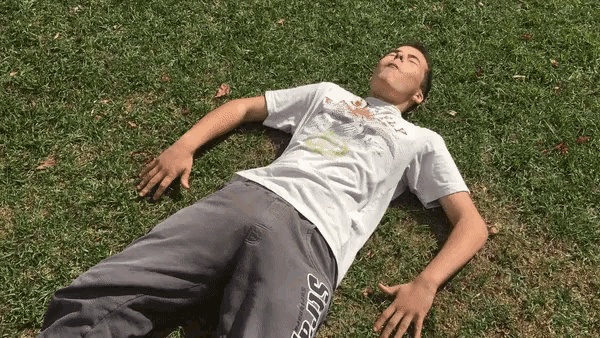 a young man laying on the grass wearing a shirt that says ' sdg ' on the side