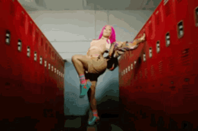 a woman with pink hair is standing in a locker room with red lockers