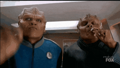 two aliens smoking cigarettes in a room with the fox logo on the screen