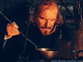 a man with a beard is holding a spoon in front of a fire and the word cannibal is on the bottom
