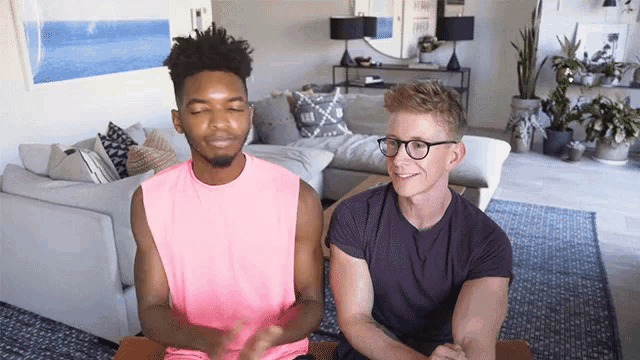 a man in a pink tank top sits next to a man in glasses