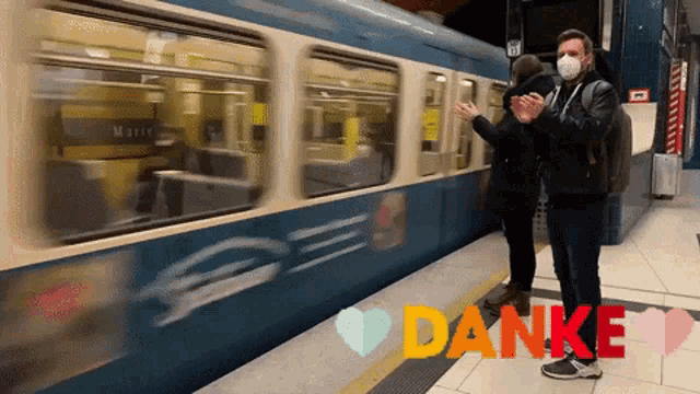 a man wearing a mask is clapping in front of a train that says danke on the bottom