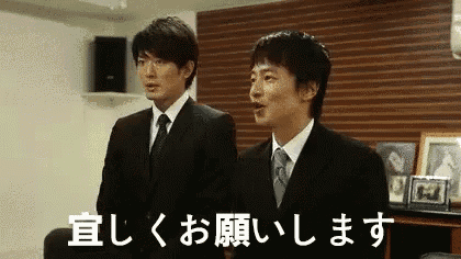 two men in suits and ties are standing next to each other in a room with chinese writing on the wall .