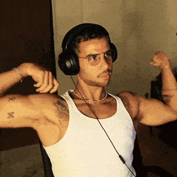 a man wearing headphones and a white tank top is flexing his muscles while listening to music .