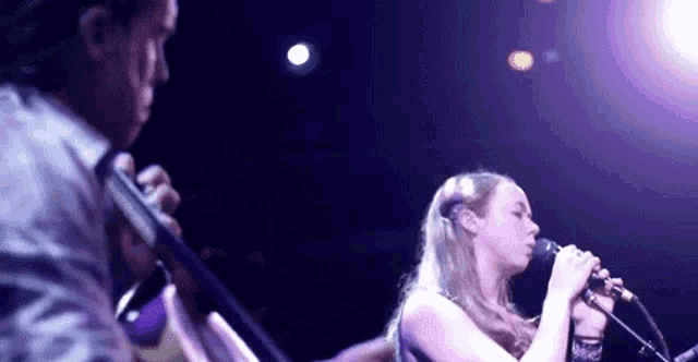 a woman is singing into a microphone while a man plays a violin on a stage .