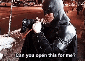 a man in a batman costume is holding a camera and asking can you open this for me