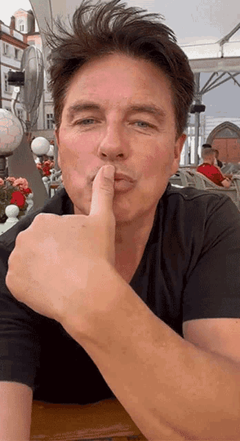a man in a black shirt is holding his finger to his mouth