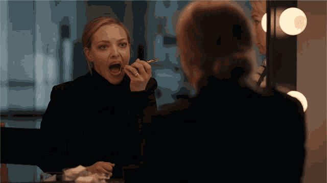 a woman applying makeup in front of a mirror with her mouth open