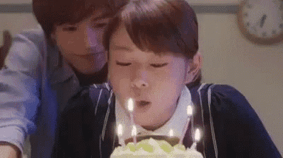 a woman is blowing out candles on a birthday cake while a man watches .