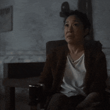 a woman in a brown sweater sits in a dark room