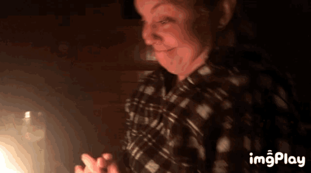 a woman in a plaid shirt is smiling in front of a lit candle with imgplay written on the bottom