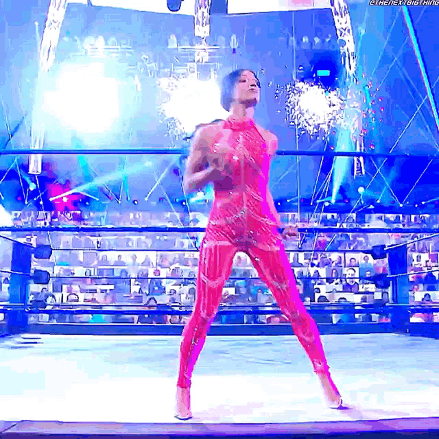 a woman in a pink bodysuit is standing in a wrestling ring with fireworks in the background