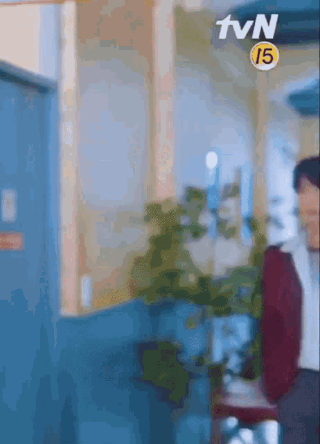 a man in a red jacket is standing in a hallway next to a tvn 15 sign .
