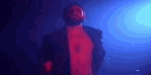 a man with a beard is standing in a dark room with his shirt off .