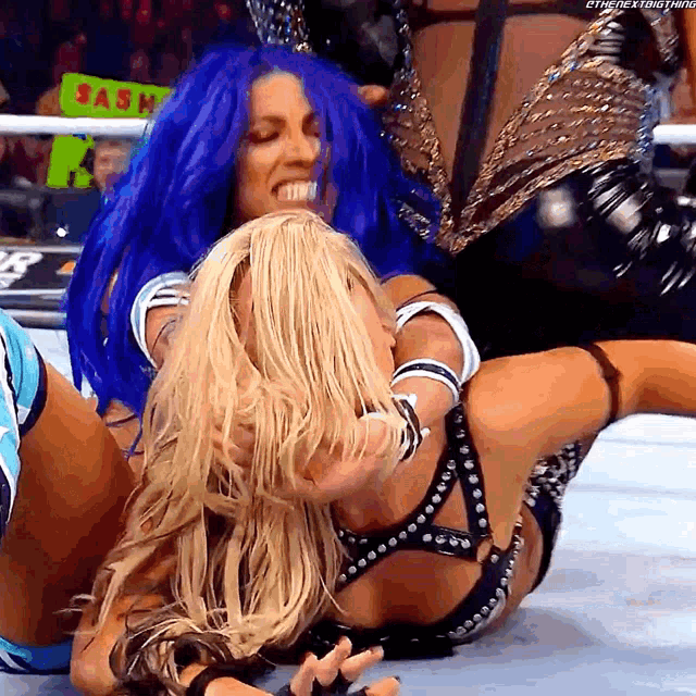 two women wrestling in a ring with a sign that says sash in the background