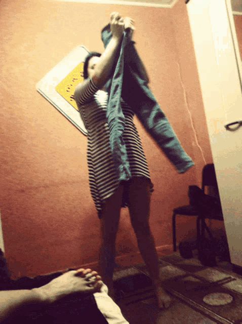 a woman in a striped dress is holding a pair of blue jeans over her head