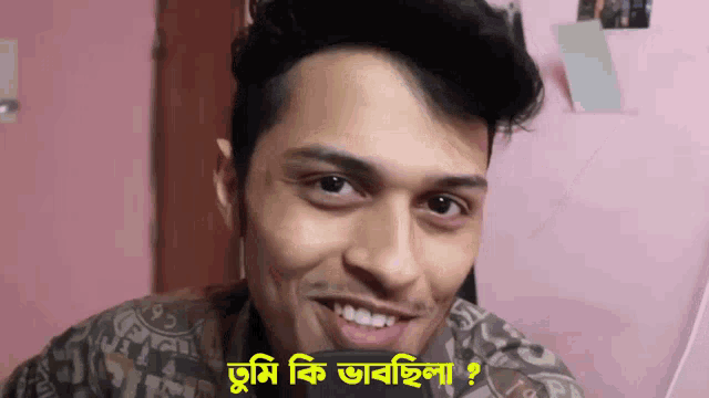 a man is smiling in front of a pink wall with a sign that says tumi ki